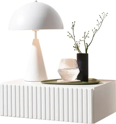 A white bedside table with a lamp, a vase with branches, and a glass of water on a tray.