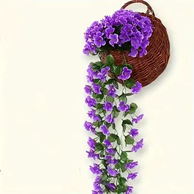Künstliche Hängepflanze mit leuchtend violetten Blüten und grünen Blättern in einem braunen Weidenkorb an einer weißen Wand