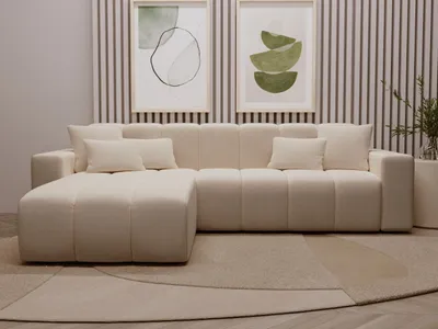 A modern beige sectional sofa with an ottoman in a living room setting, with abstract art on the wall.