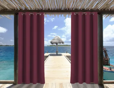 View of a tropical beach scene through an opening framed by burgundy outdoor curtains.