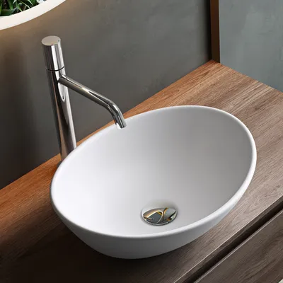 A white ceramic vessel sink with a chrome faucet on a wooden countertop.