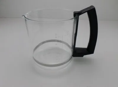 A clear glass coffee pot with a black handle rests on a white surface.