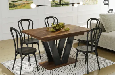 A dining table with chairs and a bowl of fruit on it, set in a dining room with a sofa in the background.