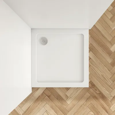 A top-down view of a white square shower tray with a drain in the corner, placed on a wooden floor with a herringbone pattern.