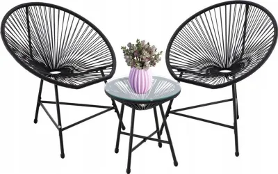 A black rattan chair and table set with a vase of flowers on the table, isolated on a white background.