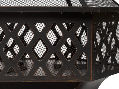 A close-up view of a dark metal fire pit with a diamond-shaped cut-out pattern and mesh backing.