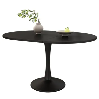 A black oval dining table with a vase of greenery and a bowl of fruit on it, set against a white background.