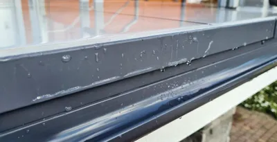 A close-up view of a dark gray aluminum gutter profile with water droplets on it.