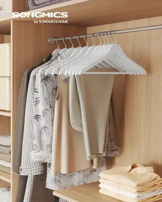 A closet interior with clothes hanging on white wooden hangers.
