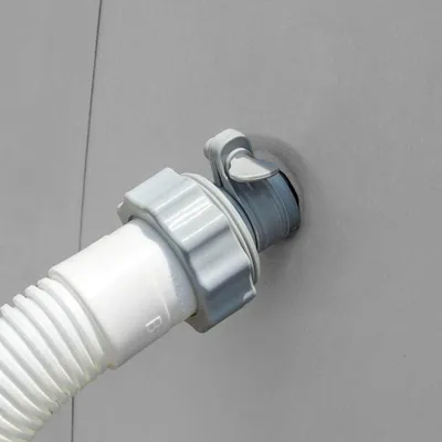 A close-up view of a white corrugated hose connected to a gray adapter fitting, which is inserted into a gray wall.