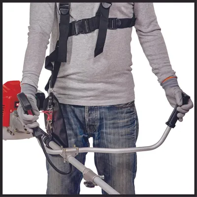 A person wearing a grey long-sleeved shirt and blue jeans, holding a string trimmer with a harness.