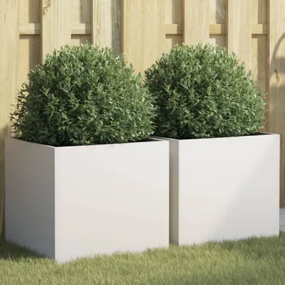 Two white square planters with green bushes in them, placed on grass in front of a wooden fence.