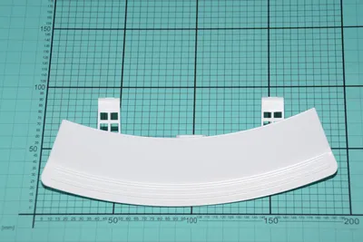 A white washing machine door handle is placed on a green cutting mat with grid lines.