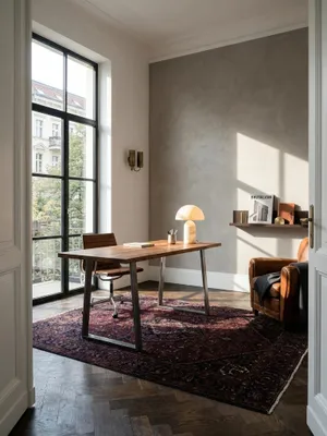 Eleganter Homeoffice-Arbeitsplatz mit einem Schreibtisch aus massivem Akazienholz mit Baumkante vor einer grauen Kalkputzwand in einem lichtdurchfluteten Altbau-Arbeitszimmer._#sku_SAFWL7.266#