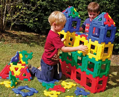 Two young boys playing with large building blocks outdoors on the grass.