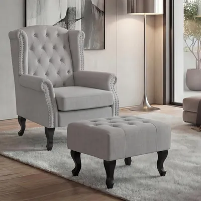 A grey armchair and ottoman are shown on a rug in a room.