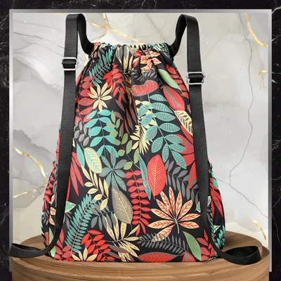 A colorful floral print drawstring backpack is displayed on a wooden surface against a marble-like background.
