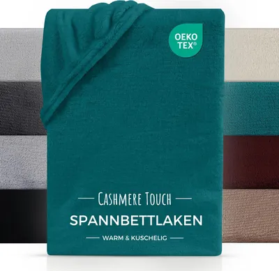 A folded teal colored bedsheet is shown in the foreground, with other colored bedsheets stacked behind it. A certification logo is visible on the bedsheet.