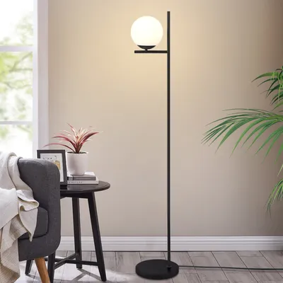 A modern floor lamp with a white globe shade stands next to a chair and a small side table with a plant and picture frame.