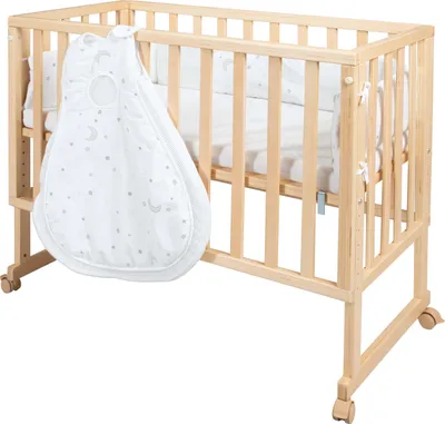 A wooden crib with a white sleeping bag hanging on the side.