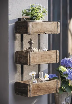 A rustic wooden wall shelf with three tiered boxes, decorated with plants and small glass bottles.