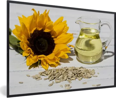 Produktbild von MuchoWow® Gerahmtes Poster Sonnenblumenkerne mit Sonnenblumenöl in einem kleinen Glas und Sonnenblume auf einem weißen Tisch 90x60 cm - Poster mit Schwarzem Bilderrahmen Wandposter Rahmen Foto Bilder - Fotorahmen - Foto-Plakat