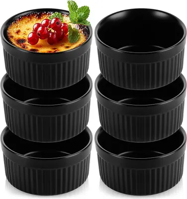 A set of black ceramic ramekins, with one filled with a crème brûlée and garnished with red currants and mint.