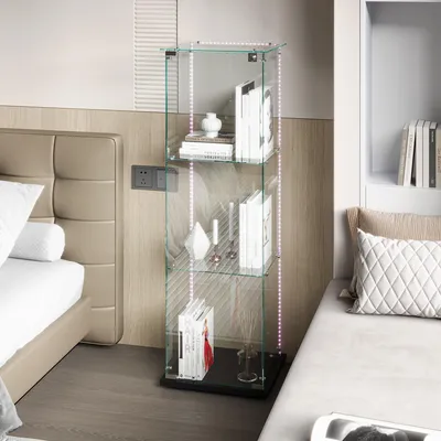 A glass display cabinet with LED lights is placed next to a bed in a bedroom.