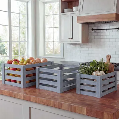 Three wooden crates filled with produce and herbs on a kitchen counter.