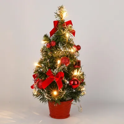 A small, decorated artificial Christmas tree with lights and red ornaments in a red pot.