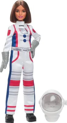 A Barbie astronaut doll standing next to her helmet.