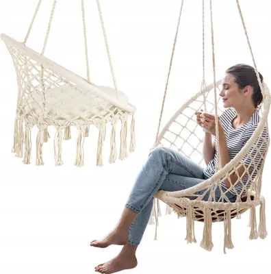 A woman sits in a macrame hanging chair, holding a mug.