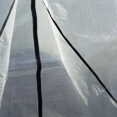 A close-up view of the material of a greenhouse tent, showing the mesh structure and zippers.