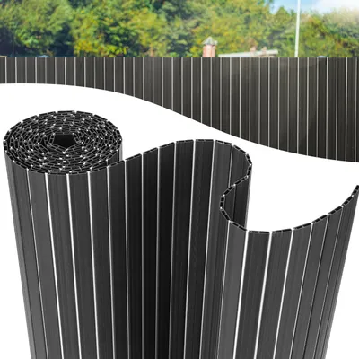 A rolled-up privacy screen is shown in the foreground, with a section of the unrolled screen extending into the background, mimicking a fence. Trees and a building are visible in the distant background.
