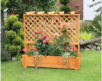 A wooden planter box with a trellis, filled with roses and other plants, sits on a green lawn in a garden setting.