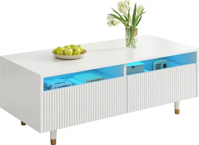 Image de Sweiko Cette table basse LED moderne dispose d'un plateau de tiroir ondulé, de pieds blancs et dorés, de deux tiroirs et d'une bande lumineuse LED à couleurs changeantes. Un meuble TV assorti est également disponible