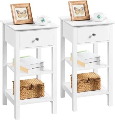 Two identical white nightstands are shown side-by-side against a white background. Each nightstand has a drawer, two open shelves, and a decorative picture frame and cup on top.