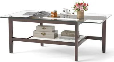 A glass-top coffee table with a wooden frame and a lower shelf, decorated with books, boxes, and a vase of flowers.