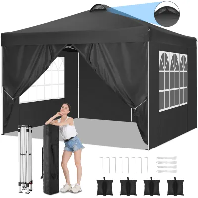 A woman is posing next to a black pop-up canopy tent. The tent is set up, and accessories like stakes and sandbags are laid out in front of it.