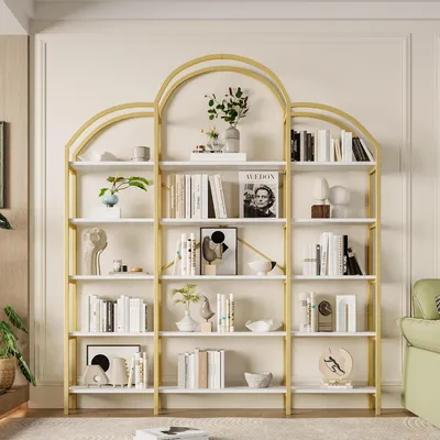 A modern, multi-shelf bookcase with a gold frame and white shelves, filled with books and decorative items, set against a neutral wall.