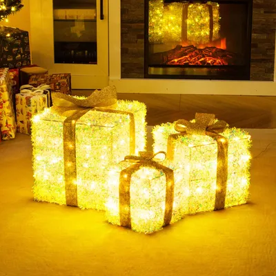 Three illuminated gift boxes with golden bows are placed on a floor in front of a fireplace and a doorway.