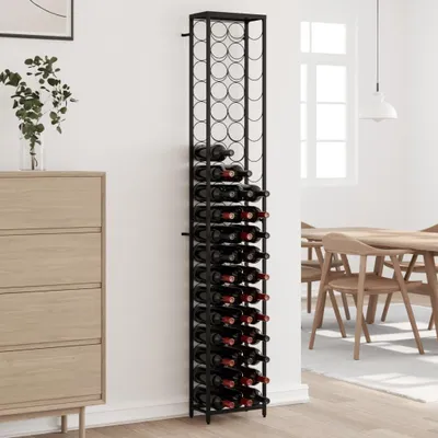 A tall, black wine rack filled with wine bottles stands against a white wall next to a wooden dresser. A dining table and chairs are visible in the background.