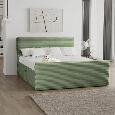 A green corduroy bed with white pillows and a white cat lying on it, in a well-lit room.