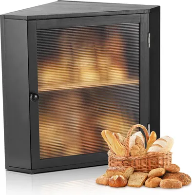 A black corner bread box with a ribbed acrylic door, filled with bread. A basket of bread and loose bread loaves are in the foreground.