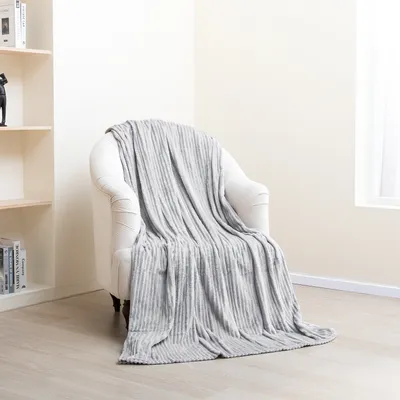 A gray blanket is draped over a white armchair in a room with light-colored walls and wooden flooring.