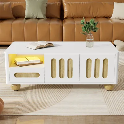 A white coffee table with wooden accents and LED lighting is placed in a living room setting, in front of a brown leather sofa.