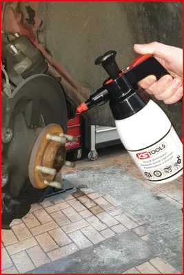 A hand is holding a spray bottle near a car's brake assembly.
