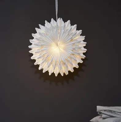 A white paper star lantern with gold glitter accents hangs against a dark gray wall.