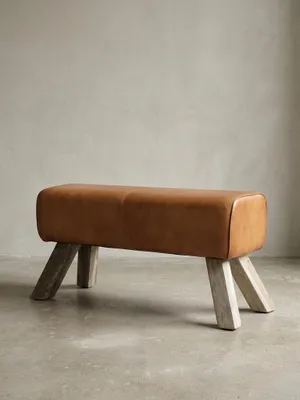 Frontalansicht der 43 cm hohen Turnbank aus cognacbraunem Ziegenleder auf weißem Hintergrund. Die vier schrägen Massivholzbeine aus hellem Mangoholz sorgen für stabilen Stand._#sku_BARWL5.105#