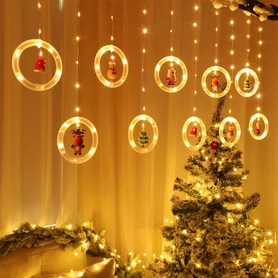 Christmas lights with decorative ornaments hanging in front of a curtain and a decorated Christmas tree.